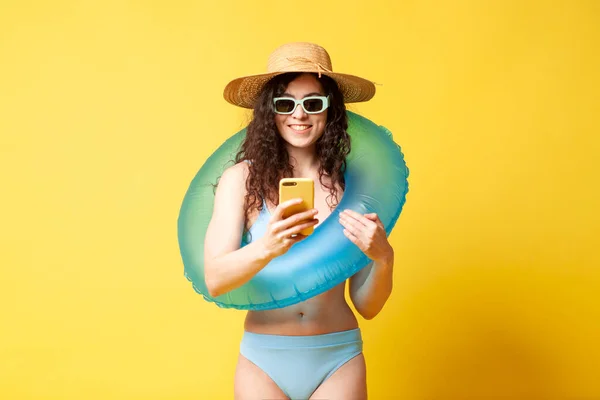 young curly girl in a blue swimsuit with an inflatable swim ring holds a smartphone in her hands and types a message, a woman on vacation in the summer uses the phone
