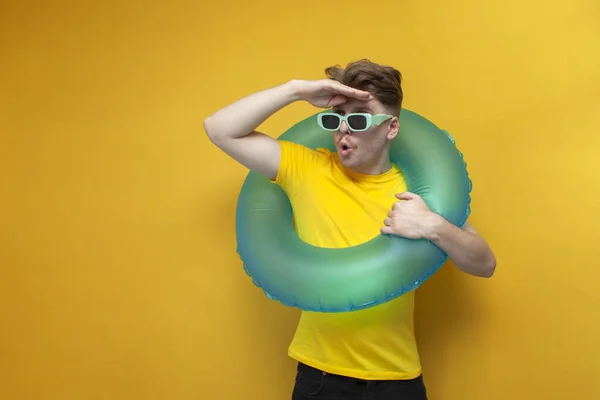 young guy in summer clothes with a swimming inflatable ring looks into the distance, the concept of traveling to the sea
