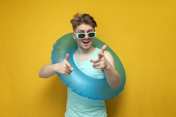 I choose you. a young guy with an inflatable swimming ring shows his hands to the camera on a yellow background, a man poses on vacation in the summer