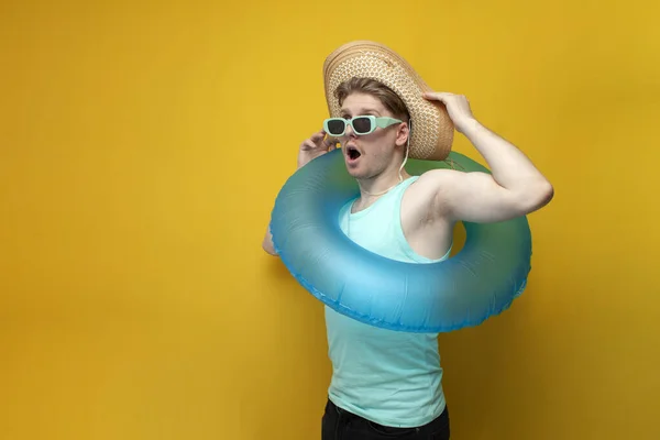 young shocked guy with an inflatable swim ring shows surprise on a yellow background, a man on vacation poses and shows emotions
