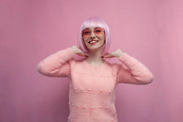 young girl with pink hair straightens her short hair and smiles on a pink background, copy space