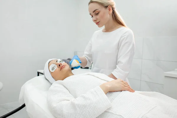 woman patient lies in a modern cosmetology clinic on a facial skin care procedure, a cosmetologist doctor works in a cosmetology room