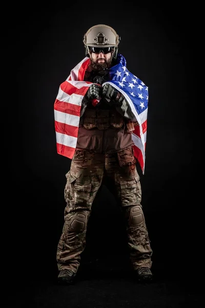 American modern special forces against a dark background, a soldier in military equipment holds weapons and the flag of the United States of America, elite troops