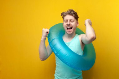 young happy guy with an inflatable swimming ring rejoices in victory and dances on a yellow background, a man rests and celebrates