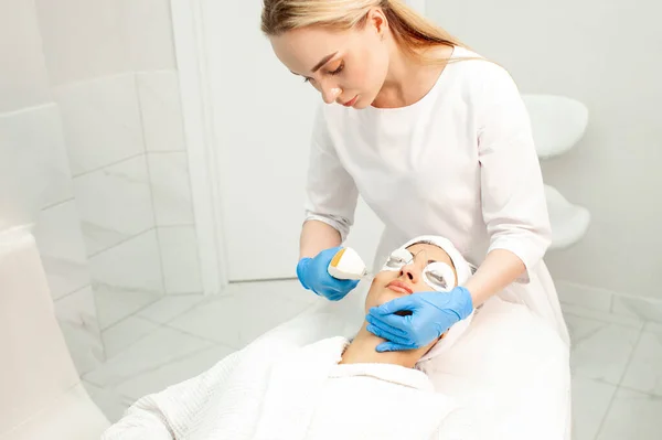 woman lies at reception in cosmetology clinic and does facial cleansing using laser and modern equipment, cosmetologist doctor makes dermatological procedure on the patient\'s face