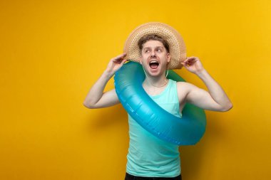 young guy in the summer on vacation with an inflatable swimming ring and a straw hat sunbathes and smiles