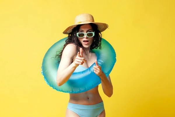 I choose you, a young girl in a blue swimsuit with a swimming inflatable ring points her fingers at the camera on a yellow background, a woman poses on vacation in the summer