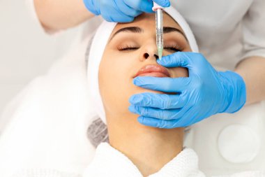 lip augmentation procedure using botox in cosmetology clinic, cosmetologist doctor in gloves makes injection with syringe in the patient's lips, close-up of syringe and needle