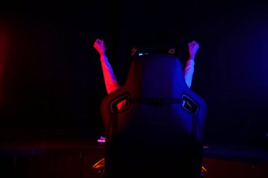 gamer plays a computer game at night and celebrates a victory, the player sits in a comfortable computer chair with his hands up, victory gesture