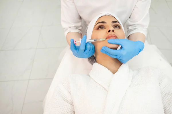 lip augmentation procedure using botox in cosmetology clinic, cosmetologist doctor in gloves makes injection with syringe in the patient's lips, close-up of syringe and needle