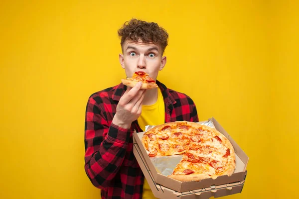 young surprised guy eating pizza on yellow background, hungry student enjoying fast food