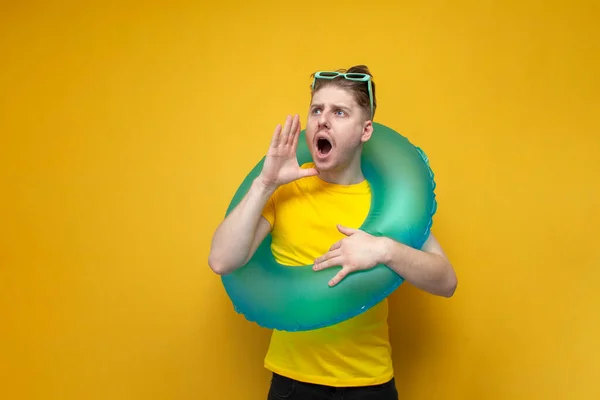young guy on vacation in the summer shouts on a yellow background, a tourist with an inflatable swim ring announces the news