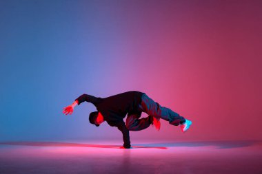 young guy dancer break dancing in neon red blue lighting, active energetic man doing acrobatic tricks, crazy moves and dancer poses