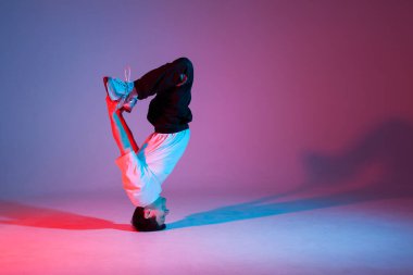 young guy dancer break dancing in neon red blue lighting, active energetic man doing acrobatic tricks, crazy moves and dancer poses