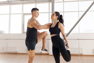 young athletic couple in training warm up in the gym in the morning, man trainer and woman do stretching exercise, copy space, healthy lifestyle