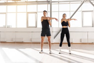 young athletic couple in training warm up in the gym in the morning, man trainer and woman do stretching exercise, copy space, healthy lifestyle