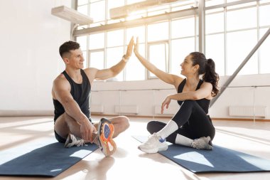 young athletic couple in sportswear in training give five with their hands, gesture of success and achievement, man coach and woman greet in the hall