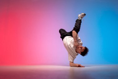 dancer doing acrobatic trick and dancing breakdance in neon red and blue lighting, young energetic guy stands on his hands in unusual pose, street style, copy space