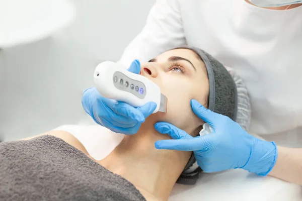 procedure of ultrasonic cavitation facial peeling. facial skin care in cosmetology clinic, woman beautician makes facial cleaning to client, close-up