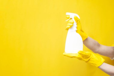 hands in yellow cleaning gloves hold detergent in bottle, empty cleaning spray in the hands of person on yellow background, copy space