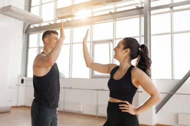 beautiful athletic couple in sportswear greet each other in the gym in the morning, fitness girl and coach man give high five in training in bright room