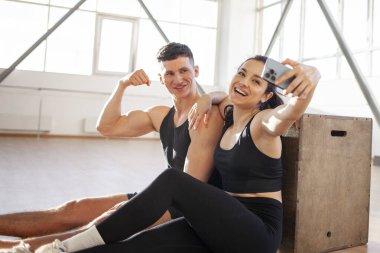 young beautiful athletic couple in sportswear in training sit and take selfie on smartphone in fitness room, woman and a man take pictures of themselves in the gym