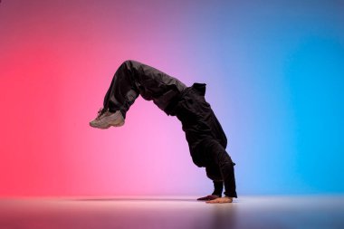 dancer doing acrobatic trick and dancing breakdance in neon red and blue lighting, young energetic guy stands on his hands in unusual pose, street style