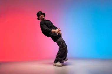 dancer dances hip hop in neon lighting, young guy moves his arms to the sides and dances break dance on red and blue background, elastic choreographer falls to the side, street rap style