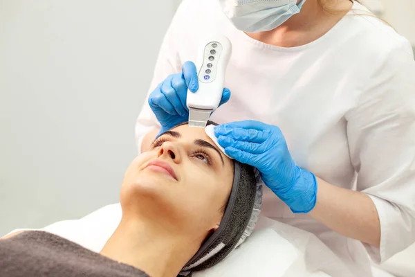 procedure of ultrasonic cavitation facial peeling. facial skin care in cosmetology clinic, woman beautician makes facial cleaning to client