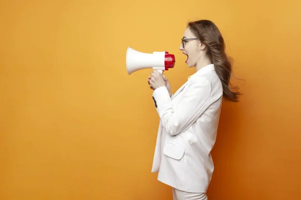 stock image young business girl in glasses and white suit announces information into megaphone on colored isolated background, female manager in office style shouts into loudspeaker