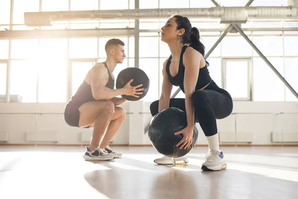 young beautiful athletic couple in sportswear at crossfit training with ball in the fitness room, woman and man together at fitness training go in for sports and do endurance exercise