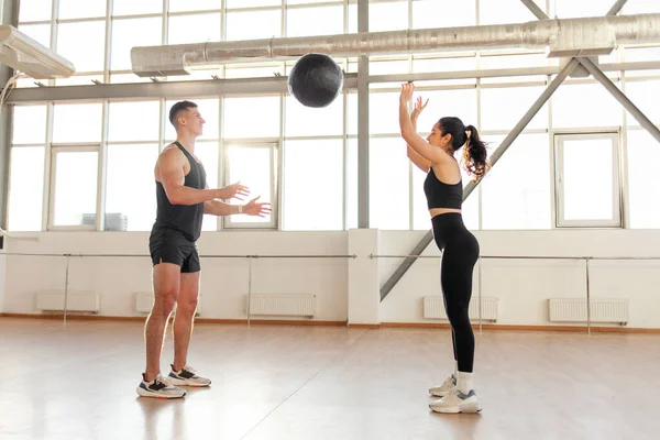 stock image young beautiful athletic couple in sportswear at crossfit training throw the ball in the fitness room, woman and man together at fitness training with ball in the morning