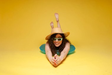 young girl in a straw hat lies on an inflatable swimming ring and shows swimming on a yellow background, a woman in the summer at the sea