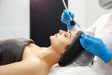 professional skin care in cosmetology clinic, dermatologist doctor applies cream with brush on the face of female patient, facial skin peeling procedure