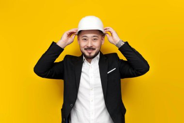 Takım elbiseli Asyalı inşaat mühendisi elinde sarı izole edilmiş arka plan planları olan evraklar, sıkı şapkalı ve iş elbiseli Koreli adam, mimar işçi