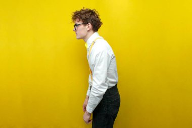 Sarı izole edilmiş arka planda kötü duruşu olan şenlikli kıyafetli genç adam papyonlu ve pantolon askısı takan inek öğrenci.