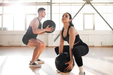 young beautiful athletic couple in sportswear at crossfit training with ball in the fitness room, woman and man together at fitness training go in for sports and do endurance exercise