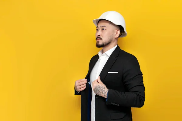 Asian civil engineer in suit holds papers with blueprints on yellow isolated background, Korean man in hard hat and business clothes, architect worker