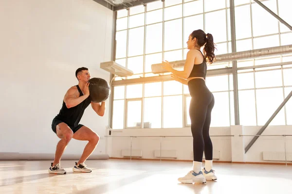 stock image young beautiful athletic couple in sportswear at crossfit training throw the ball in the fitness room, woman and man together at fitness training with ball in the morning