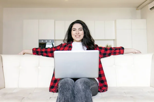 若い巻き女性は快適なソファの上に家に座って ラップトップを使用して 女の子はソファの上でコンピュータで作業し 映画を見て — ストック写真