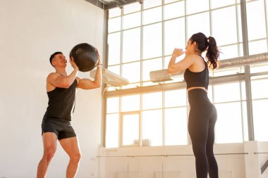 young beautiful athletic couple in sportswear at crossfit training throw the ball in the fitness room, woman and man together at fitness training with ball in the morning