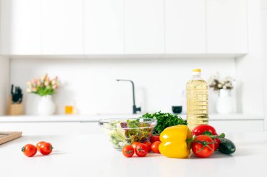 Salata ve ürünler için malzemeler beyaz modern mutfakta, yeşillikler, domatesler, biberler, boş mutfakta bir şişe yağ, sağlıklı vejetaryen yiyecekler.