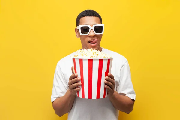 若いですかわいい男アフリカ系アメリカ人はポップコーンを食べ 黄色の隔離された背景に映画を見ます 満足男映画鑑賞者笑顔 — ストック写真