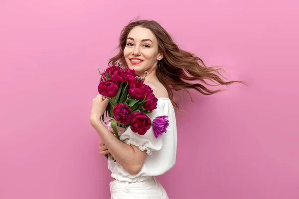 stock image young attractive woman in white festive clothes holding bouquet of pink tulips and swirl on isolated background, girl moves with flowers and her hair is flying, concept of spring and women's holiday