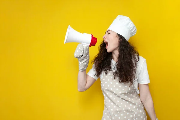 穿着围裙和烘焙手套的女厨师拿着扩音器 在黄色孤立的背景上播报消息 身着制服的家庭主妇对着扩音器高喊 — 图库照片