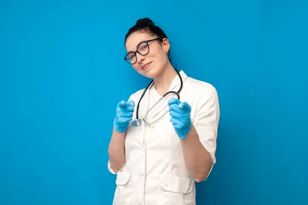 I choose you. doctor woman in uniform shows her hands to the camera on blue background, girl nurse in medical gown chooses you