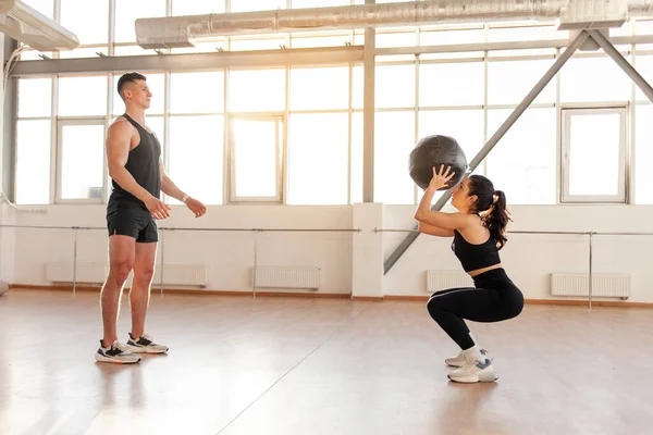 stock image young beautiful athletic couple in sportswear at crossfit training throw the ball in the fitness room, woman and man together at fitness training with ball in the morning