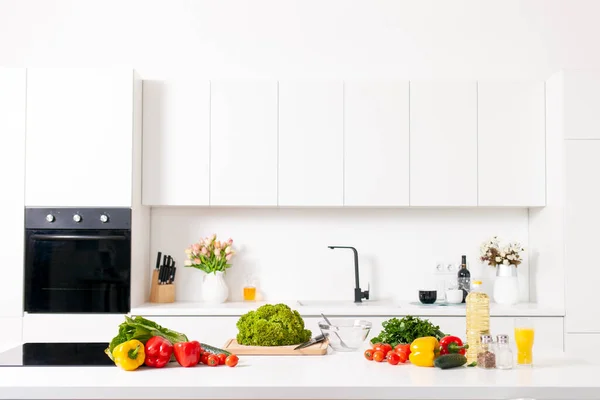 stock image ingredients for salad and products lie on the table in white modern kitchen, the interior of light kitchen without people with greens and products for healthy vegetarian meal, copy space