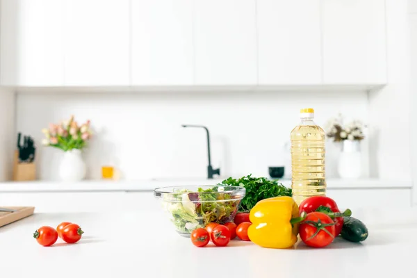 stock image ingredients for salad and products lie on the table in white modern kitchen, greens, tomatoes, peppers, bottle of oil in empty light kitchen, healthy vegetarian food