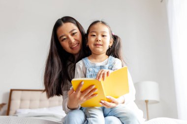 Asyalı anne kızına evde yatakta okuma yazma öğretiyor. Küçük Koreli kız not defterine ebeveynleri, aile eğitimi ve yetiştirme eğitimi ile birlikte yazıyor.